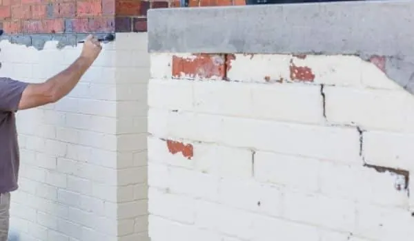 A painter rolling white paint onto an exterior brick wall