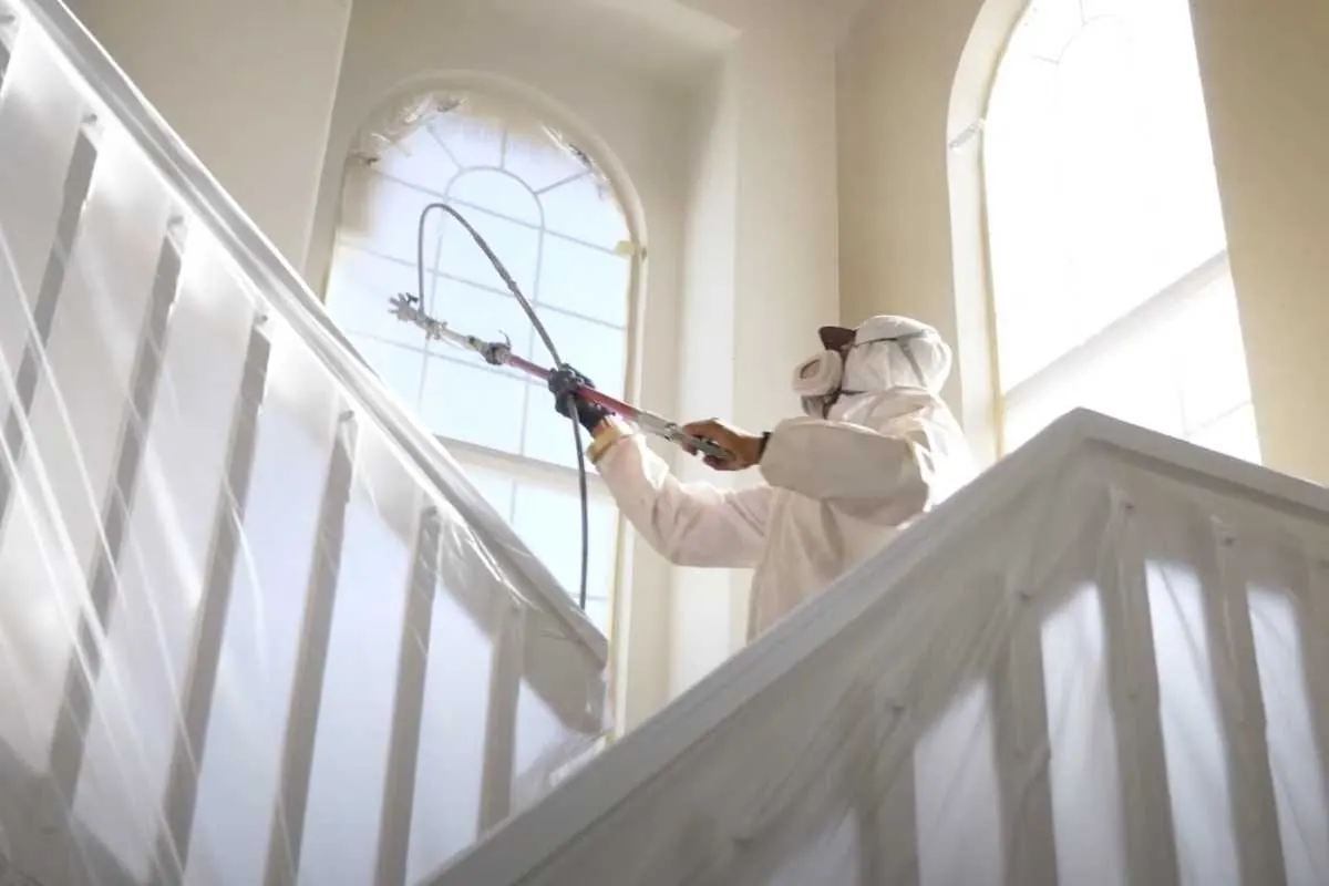 A Kind Home painter spraying a staircase in full protective gear